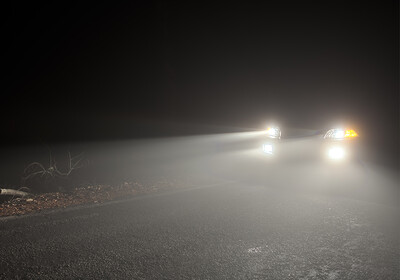 Ein Auto fährt nachts mit eingeschaltetem Abblendlicht durch dichten Nebel auf einer Landstraße.